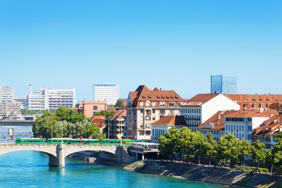 Bridge over river by buildings against clear blue sky