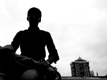 Low angle view of man sitting on building against sky