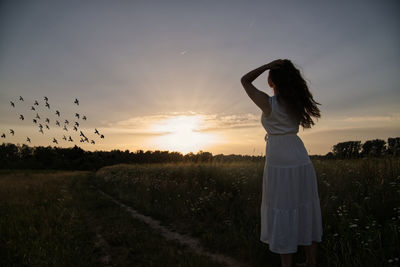 Woman standing on field against sky during sunset
