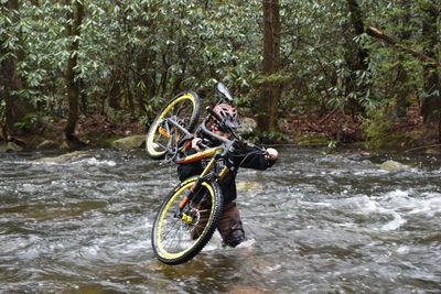 Bicyclist carrying motorbike in river at forest