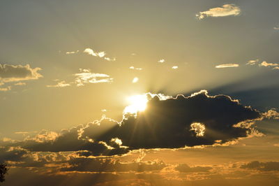 Low angle view of sunlight streaming through clouds during sunset