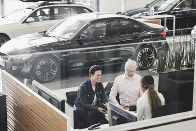 High angle view of saleswoman discussing with customers at car showroom