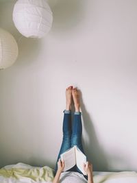 Woman lying on bed reading book with legs raised