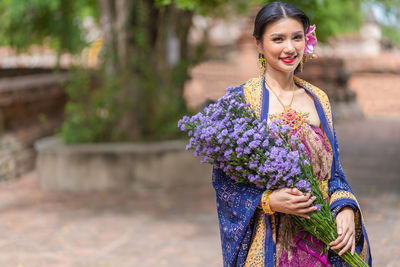 Portrait of smiling woman wearing traditional clothing holding flowers standing outdoors