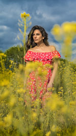 Young woman standing amidst flowers against cloudy sky