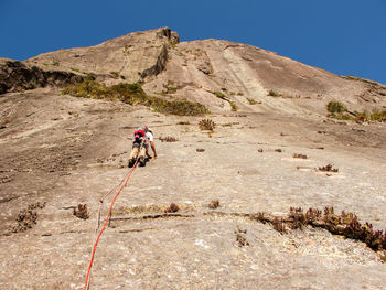Man standing on rock by mountain against clear sky