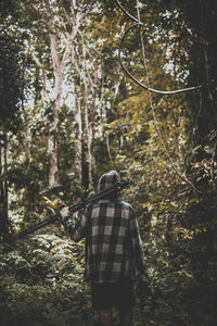 Rear view of man holding tripod while standing in forest