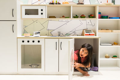 Portrait of smiling girl hiding under shelf