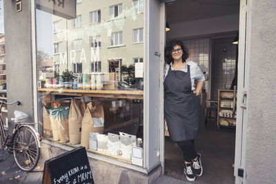 Full length of smiling female owner standing at organic store doorway