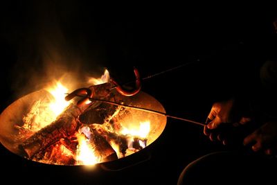 Cropped hand preparing sausage in bonfire at night