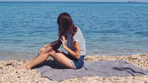 Woman sitting on beach by sea