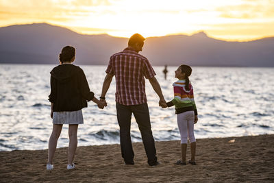 A dad and his daughters watch sunset on the beach in lake tahoe, nv