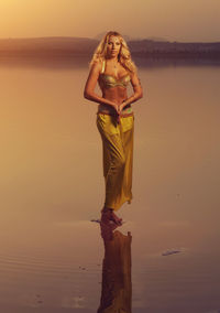 Portrait of young woman standing at beach during sunset