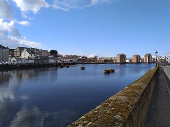 Buildings by river against blue sky