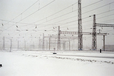 Electricity pylons over railroad tracks against sky