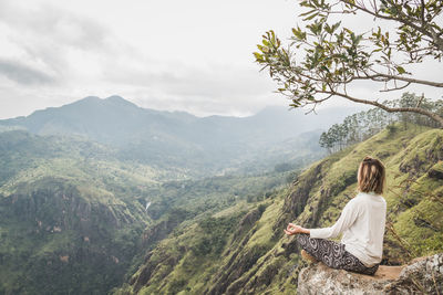 Woman sitting on mountain against sky