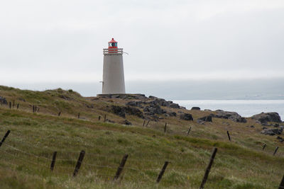 Lighthouse on landscape by sea against sky
