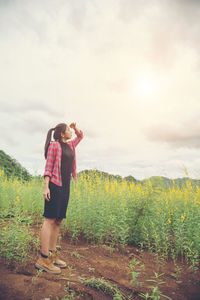 Woman shielding eyes while standing on field against sky