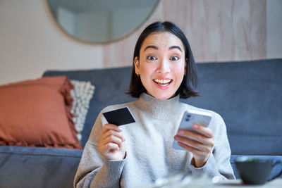 Young woman using mobile phone while sitting on sofa at home