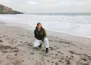 Full length of man sitting on shore at beach against sky