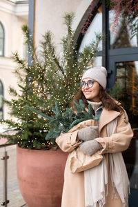 A stylish young woman in a hat with branches of nobilis leaves a cafe decorated for christmas