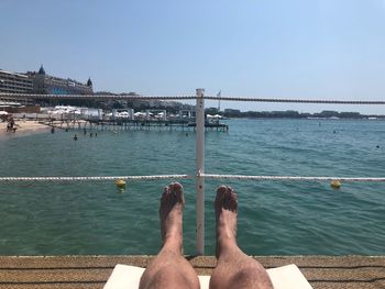Low section of man in swimming pool by sea against sky