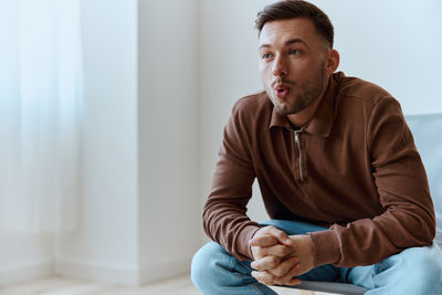 Portrait of young man sitting on bed at home