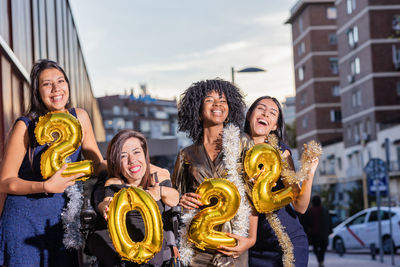 Cheerful friends holding balloons standing on street