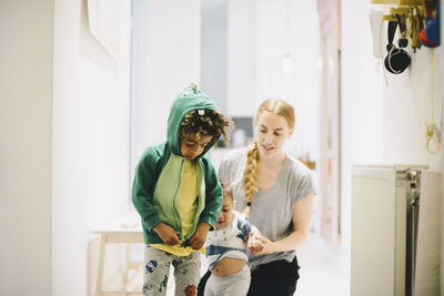 Mother with son looking at boy zipping jacket at home