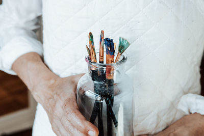 Midsection of person holding paintbrushes