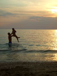 Man surfing in sea against sky during sunset