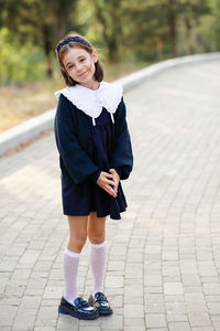 Pretty smiling school child girl 6-7 year old wear stylish unifort posing outdoor in park. 