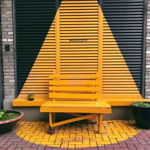 Empty bench against yellow building