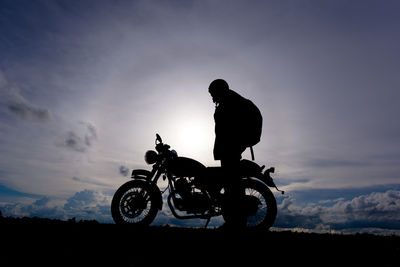 Silhouette biker with motorcycle standing on landscape against sky during sunset