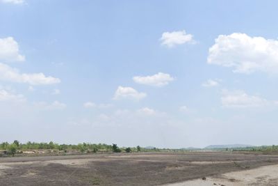 Dirt road amidst field against sky