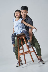 Father holding daughter sitting on table against white background