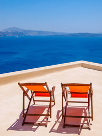 Chairs and table by swimming pool against sea