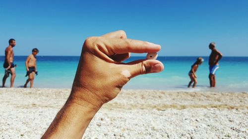 Hand holding rock on pebble beach with people in the background