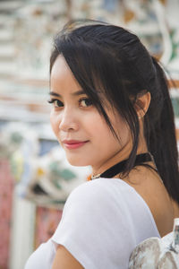 An asian woman in a white t-shirt looking at a camera with a budhist temple building background