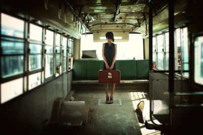 Full length of woman holding briefcase while standing in bus