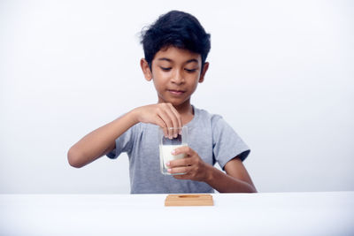 Portrait of young woman using mobile phone while sitting on table against white background