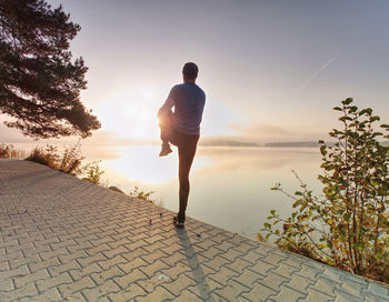 Runner stretching leg in front of river. athletic sport man stretching leg muscles before run 