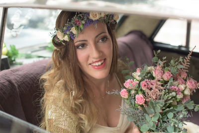 Smiling bride with flower bouquet sitting in car