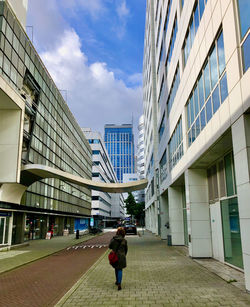 Rear view of woman walking on footpath amidst buildings in city