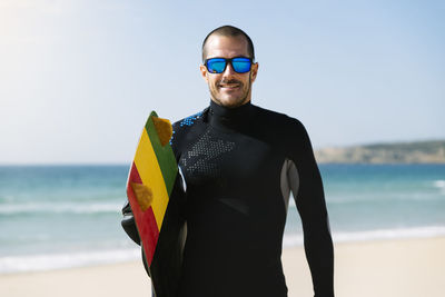 Portrait of young man with surfboard standing on beach
