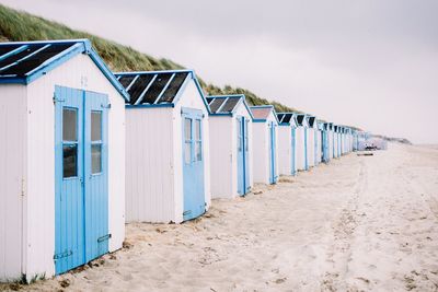 Huts in row at sandy beach against sky