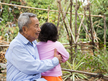 Side view of senior man holding granddaughter in yard 