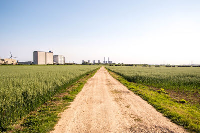 Dirt road amidst field against clear sky