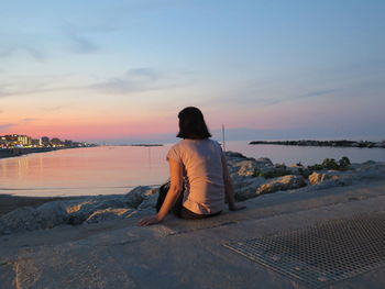 Rear view of woman sitting on shore at sunset