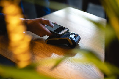 Man doing online payment through smart phone over credit card reader at cafe